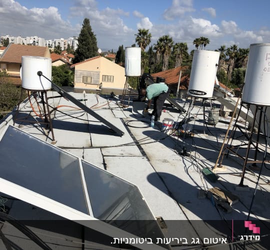 אדם עובד על איטום גג עם דליים וכלים